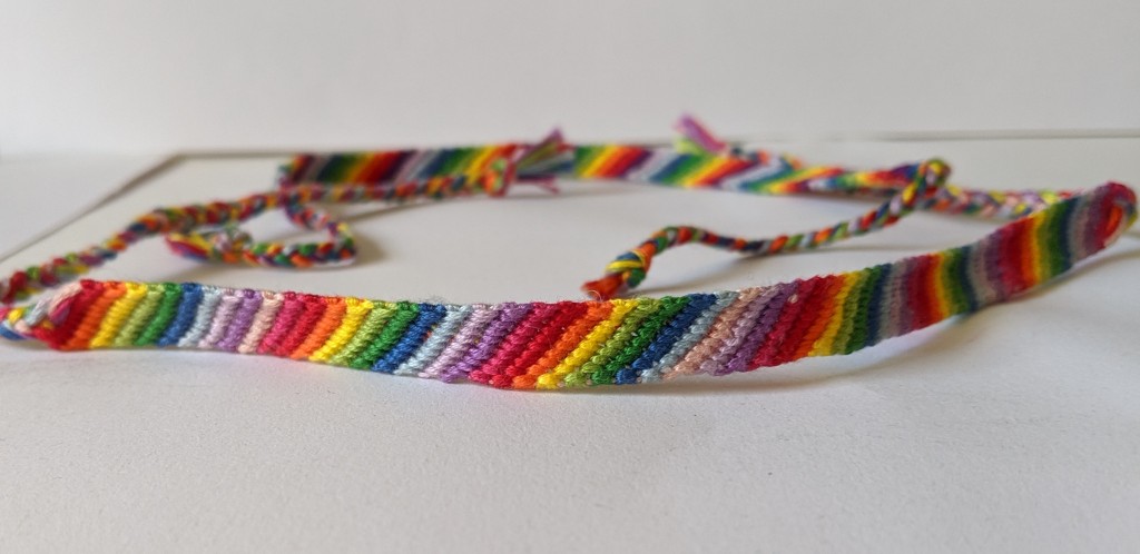 Rainbow friendship bracelets. Diagonal design going from left to right. This image shows a close up of the design to show the darker and lighter reds, blues, greens and an orange and yellow and darker and lighter purple and pink.